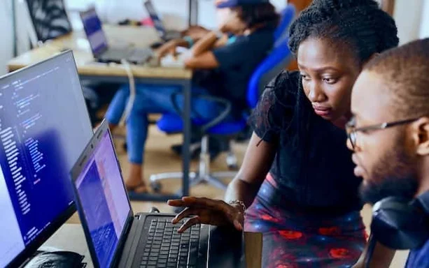 A woman teaching a man how to do something on the computer